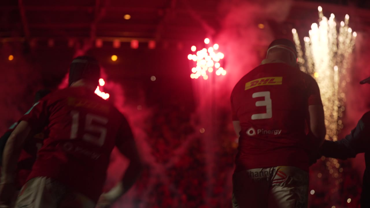 Players walking out through pyro under floodlights